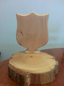 Picture of wooden sculpture - a Salvation Army Shield carved from Huon Pine on a disc of Huon Pine. Made by Ben Clapton